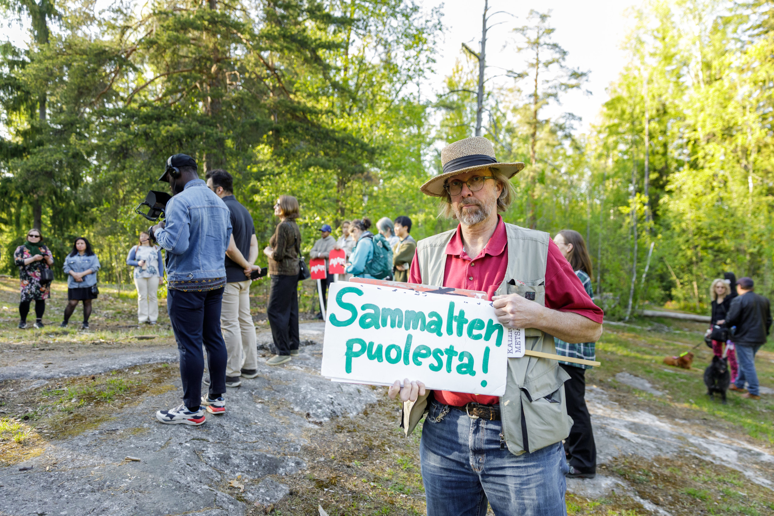 Man with a hat holding a sign saying "For the mosses" in Finnish.