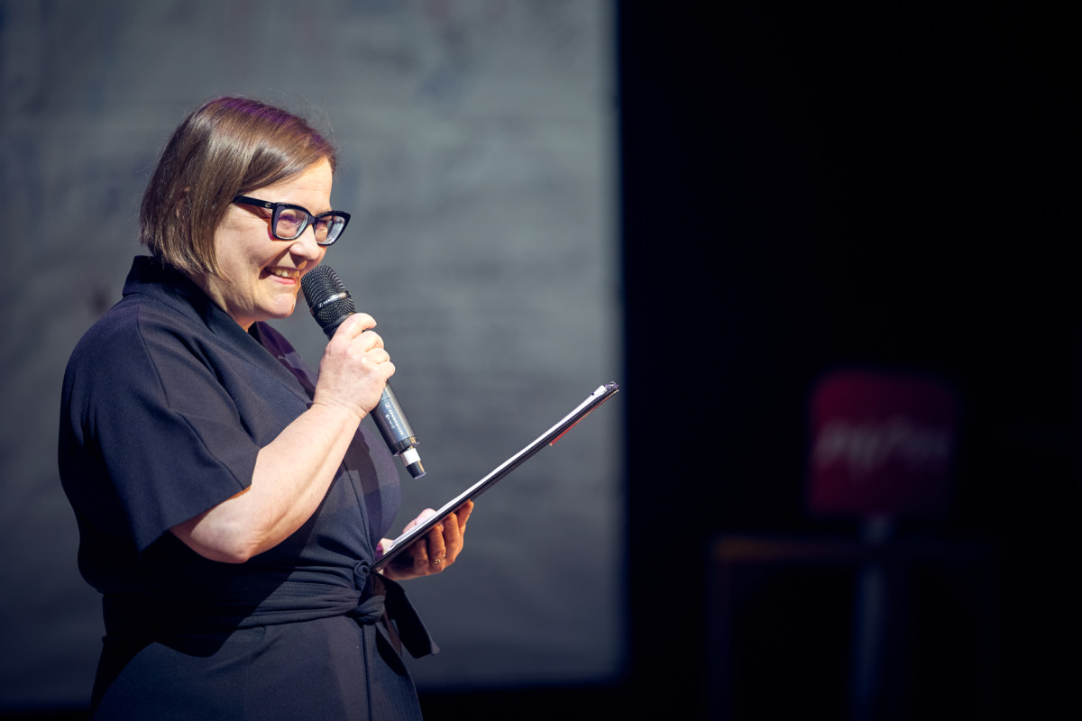 Advisory Board member Paula Toppila, woman smiling with glasses and speaking to a microphone.