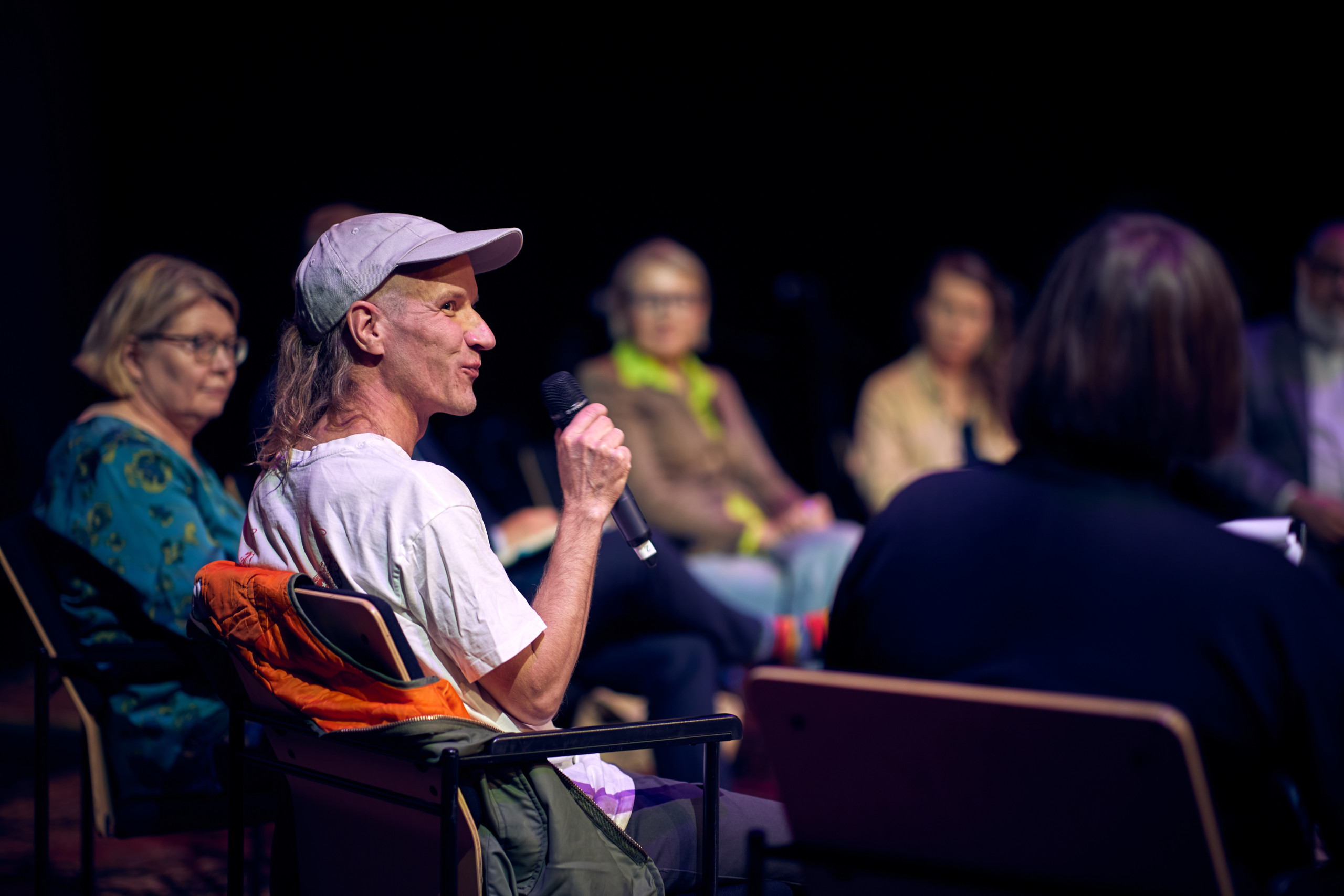 A man in a cap smiling and speaking to a microphone.