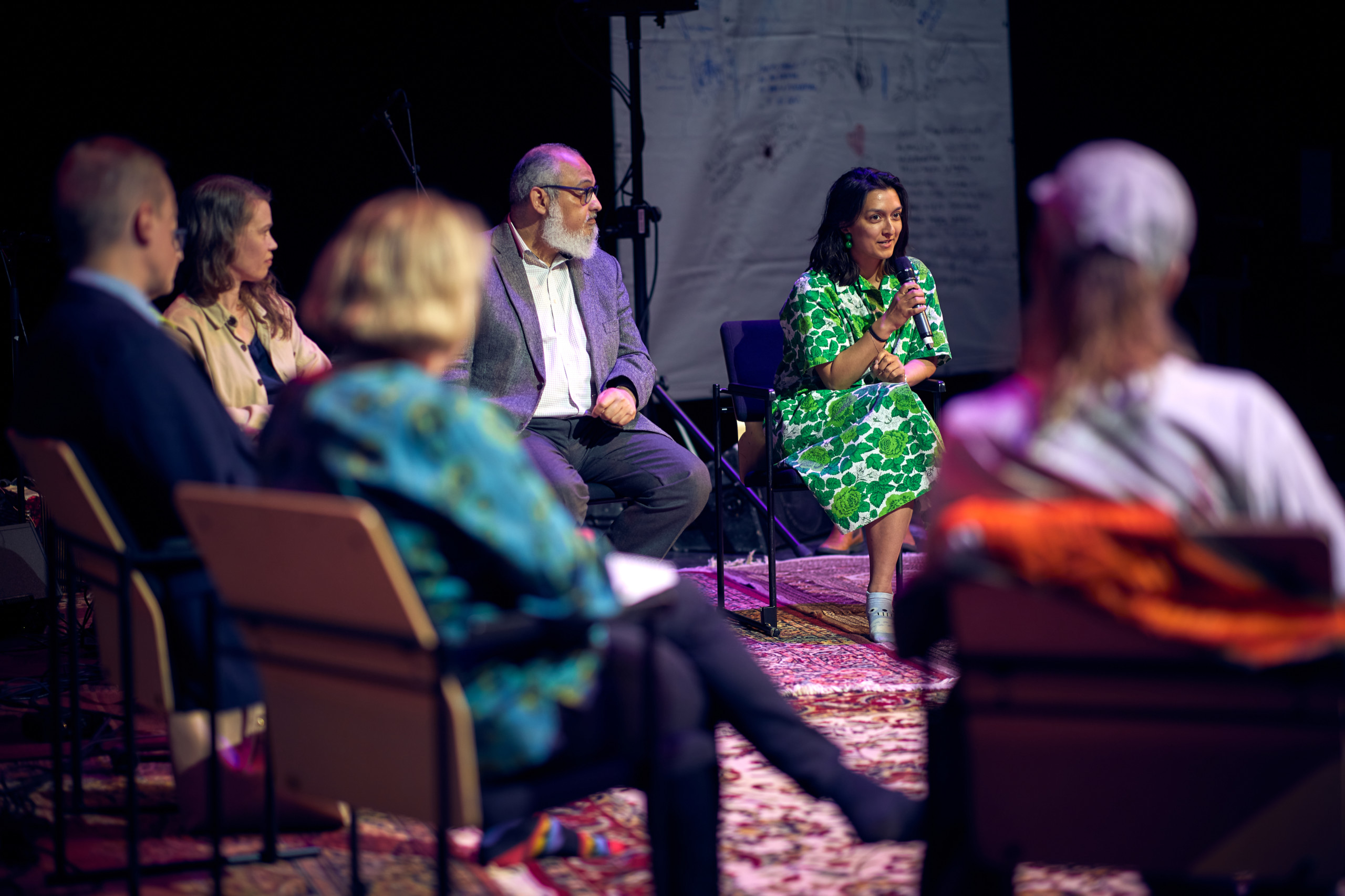 Group of people sitting and one speaking to a microphone.