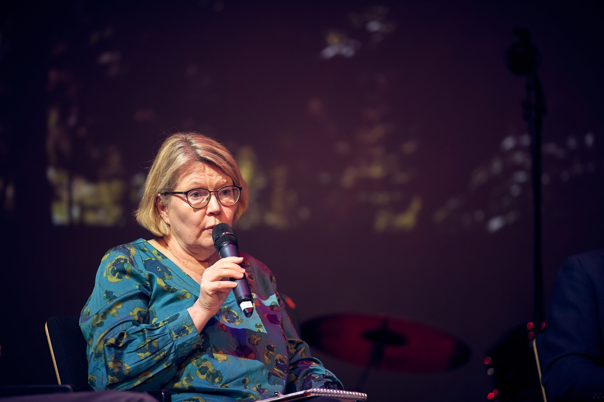 A woman in glasses speaking to a microphone.