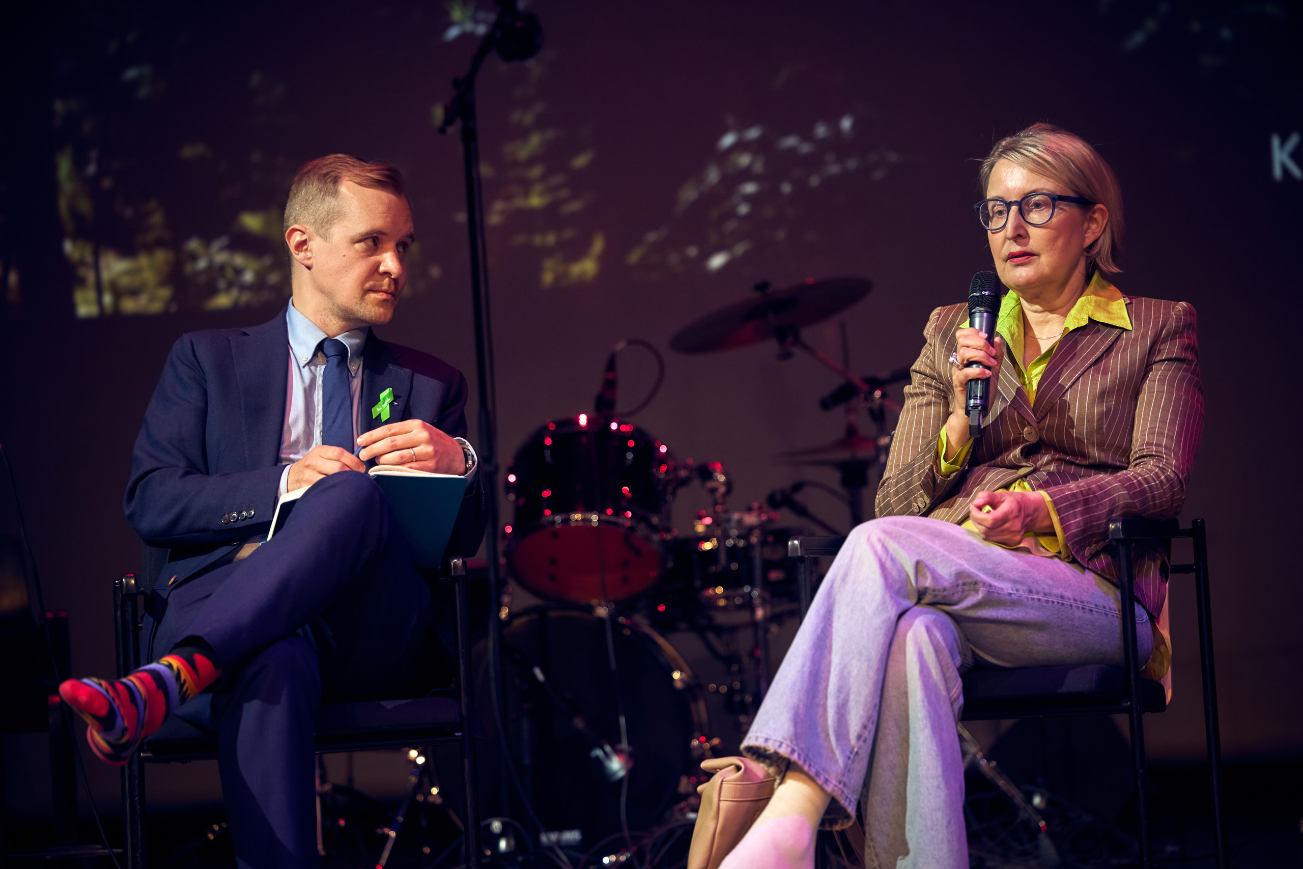 A man in blue suit and a woman in a jacket and jeans discussing.