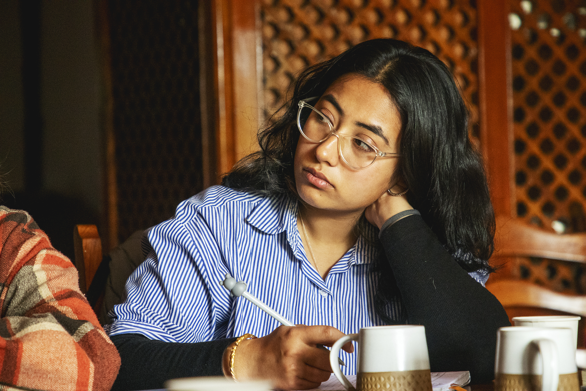 A young female in glasses listening concentrated and leaning on her hand.