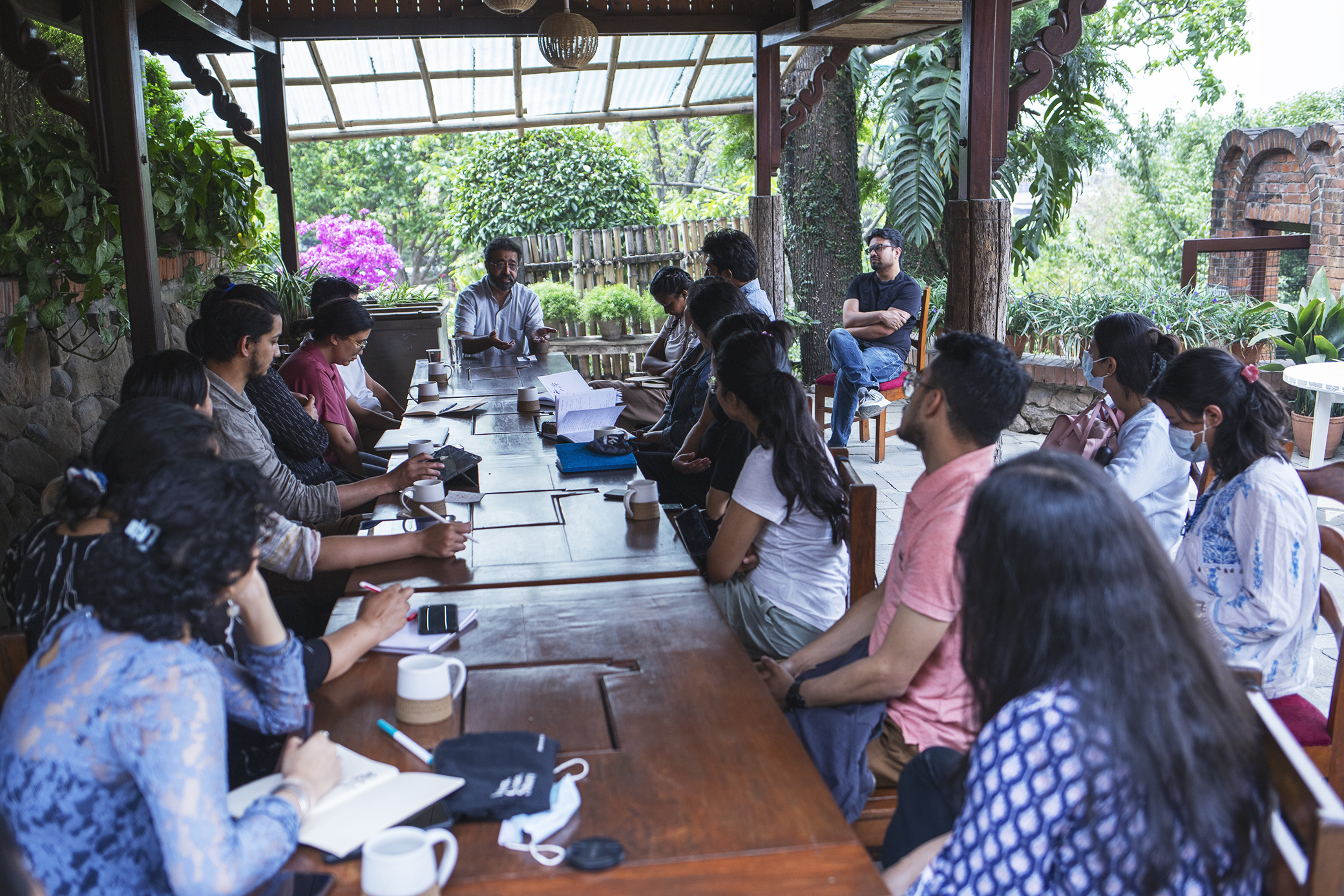 A group of people around a long table listening to Amar Kanwar at the Learning from Doubt course in Nepal.