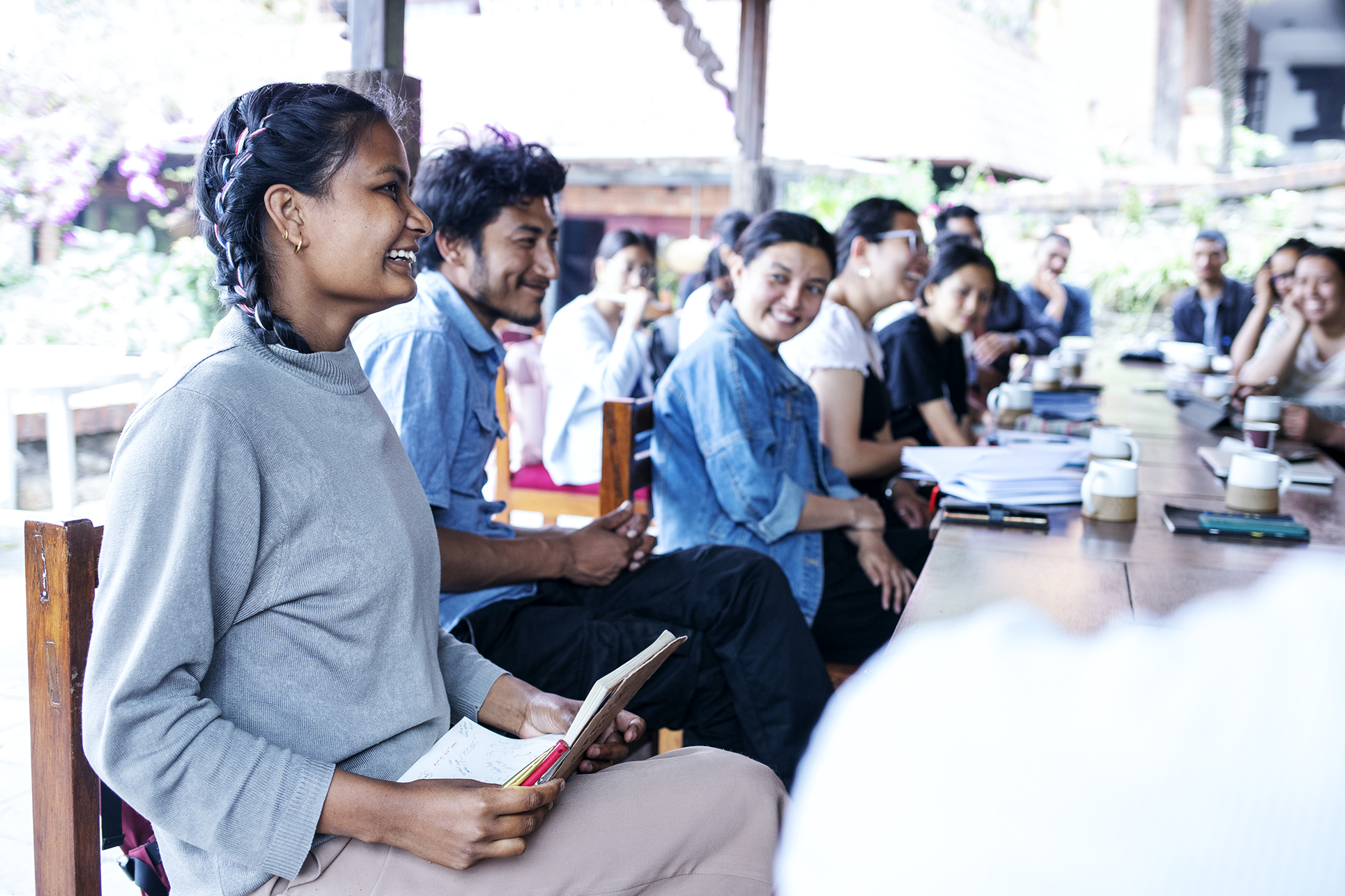 A group of students smiling and laughing around a table at the Learning from Doubt course in Nepal.