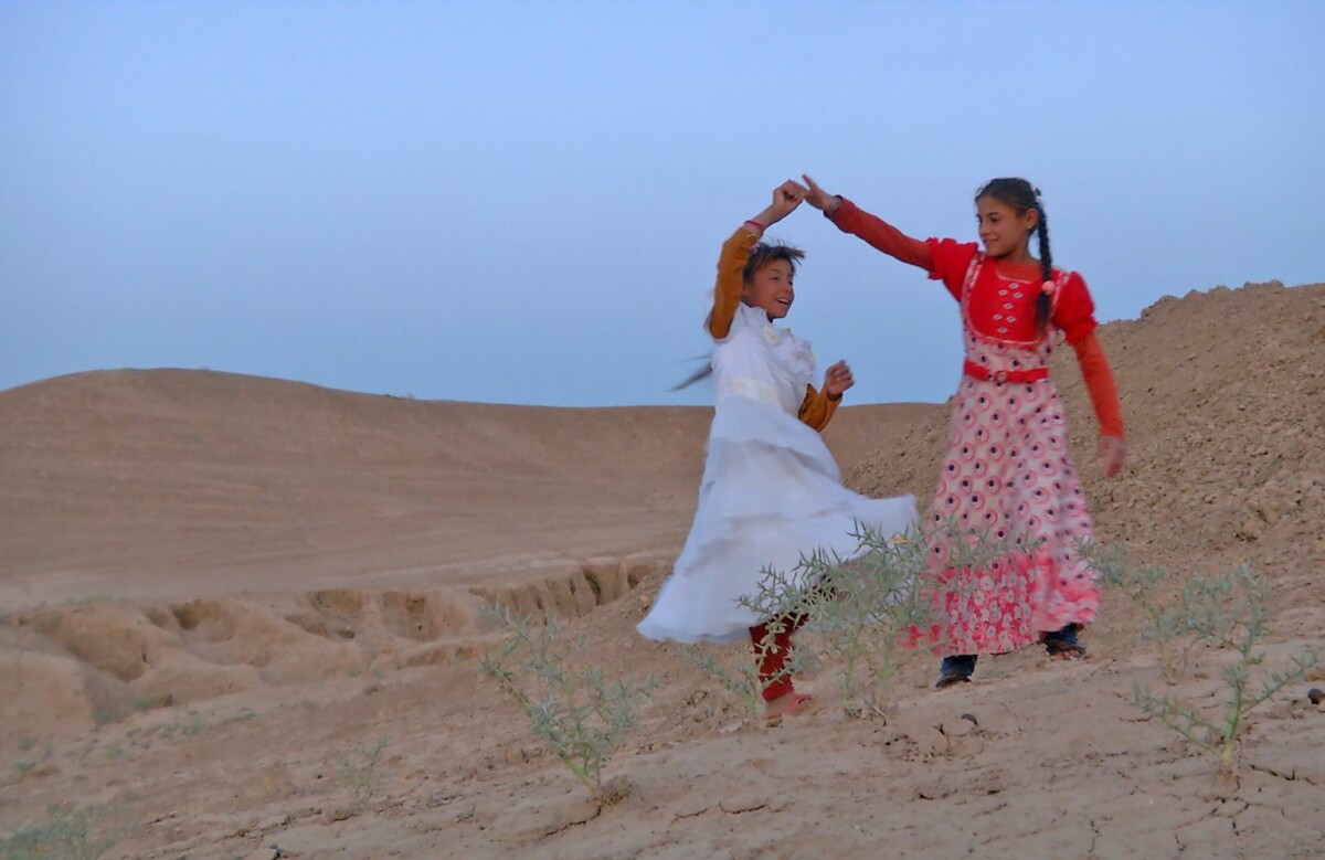 Two girls with long dresses dancing in a desert.