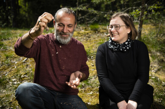 Laughing man with a beard and a smiling woman in glasses sittin outside in the woods.