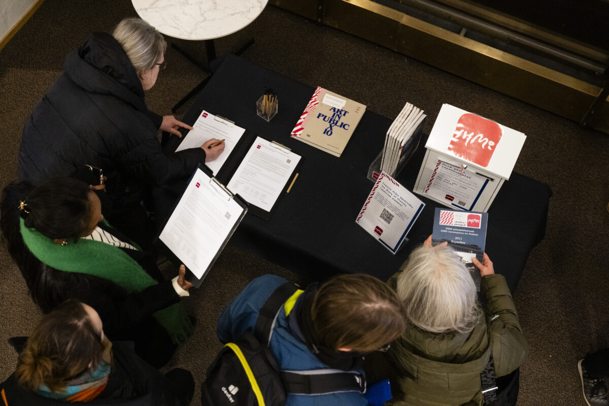 Image of people gathered around a table at the lobby of the cinema and going through material about IHME Helsinki and filling feedback forms.