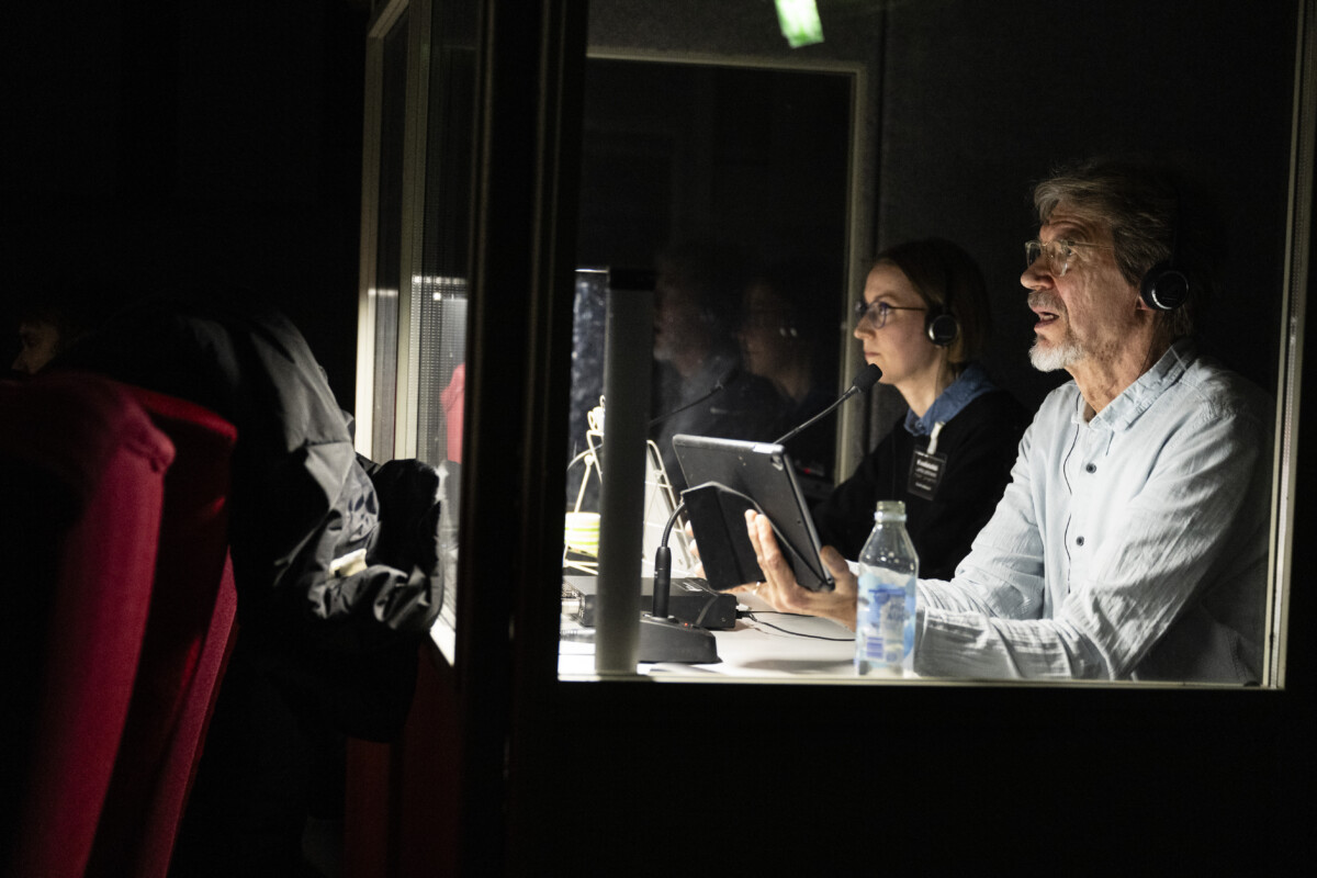 Image of a two people sitting in a lighted cubicle and working for the audio description.