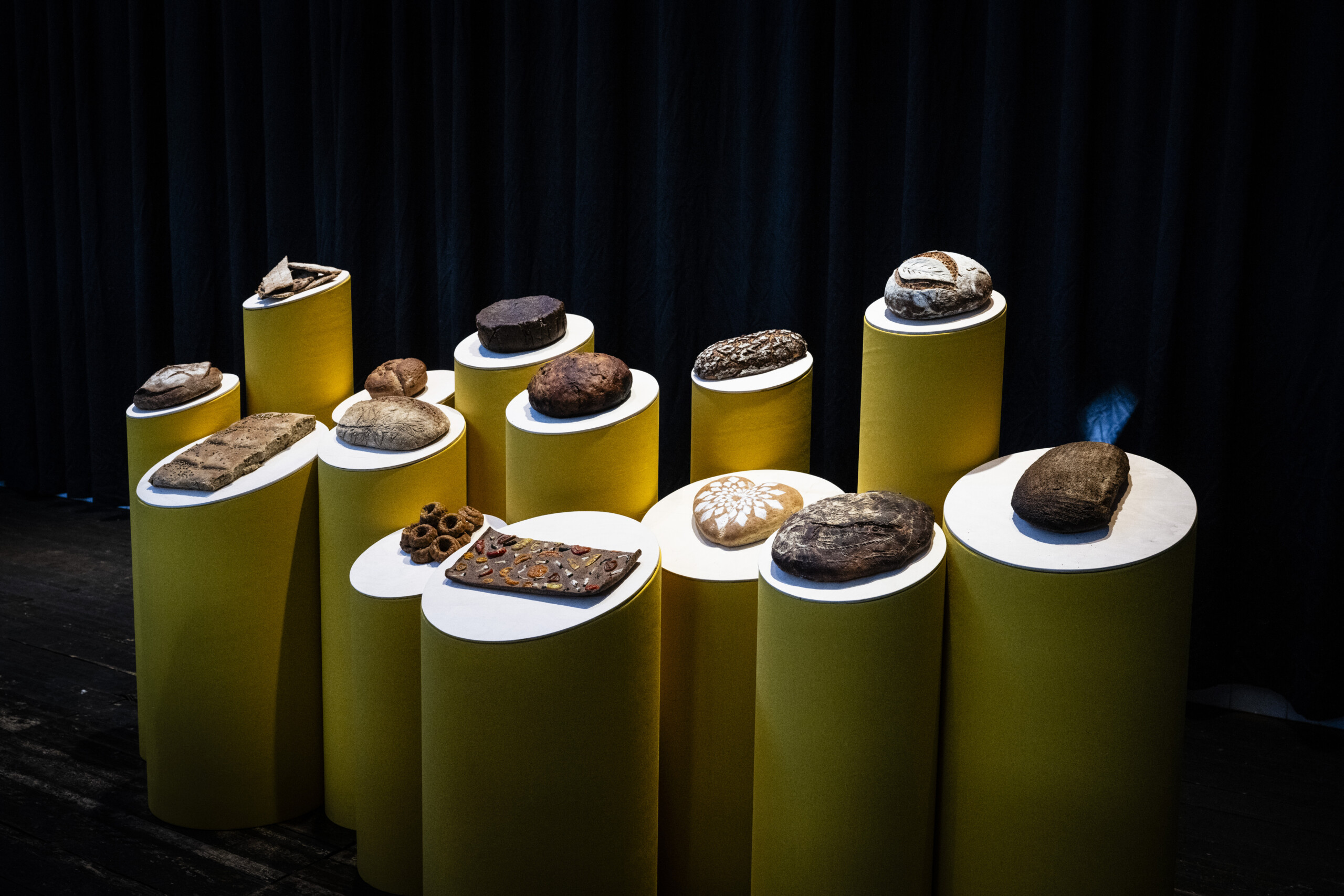 Image of a group of breads displayed on a stage. The breads are placed on yellow round stands.