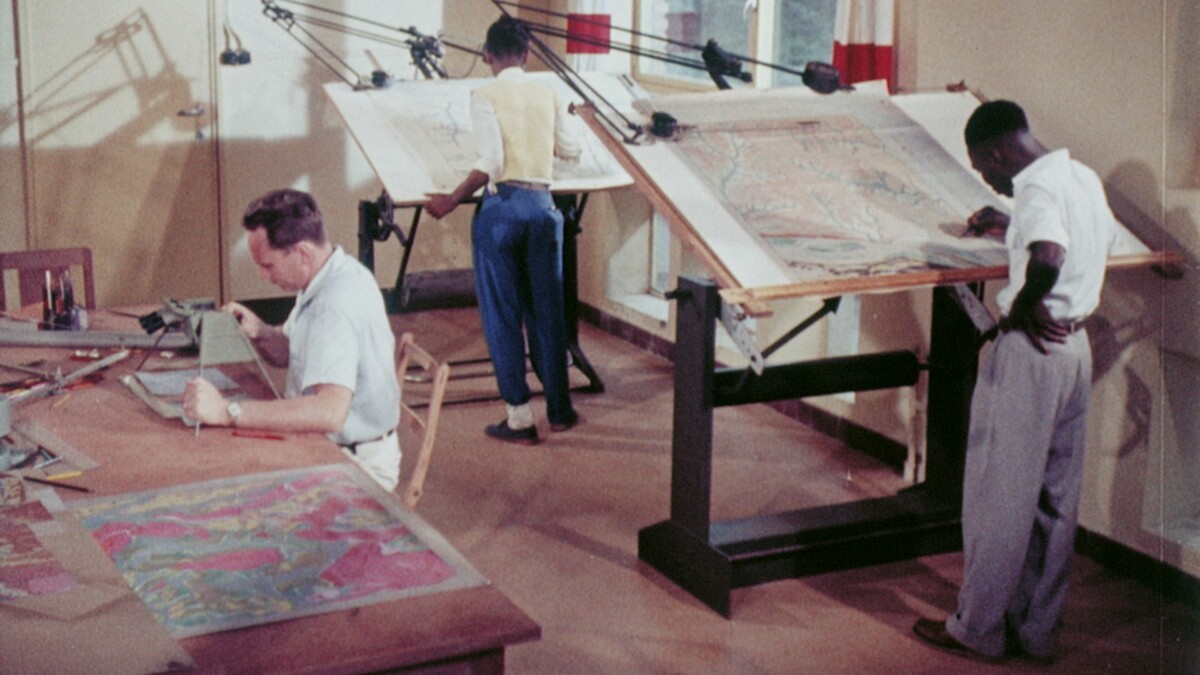 An archive photo of an office where three men, one white and two dark-skinned, are working on various maps.