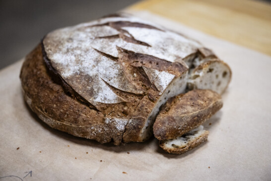 Image of a round, crusty and light brown sourdough bread that has one slice cut off.